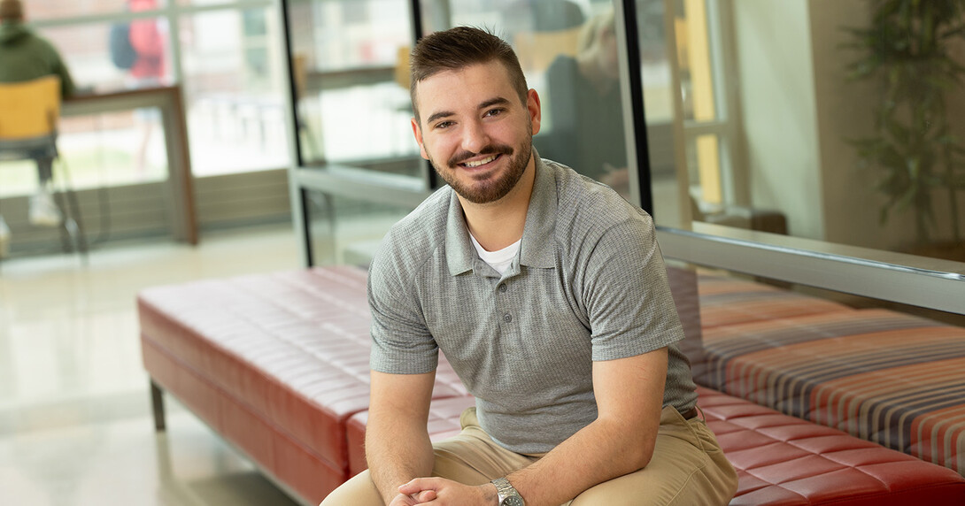 Baden Brumbaugh sits in a grey shirt and khakis, with his hands together and with short brown hair and a beard.