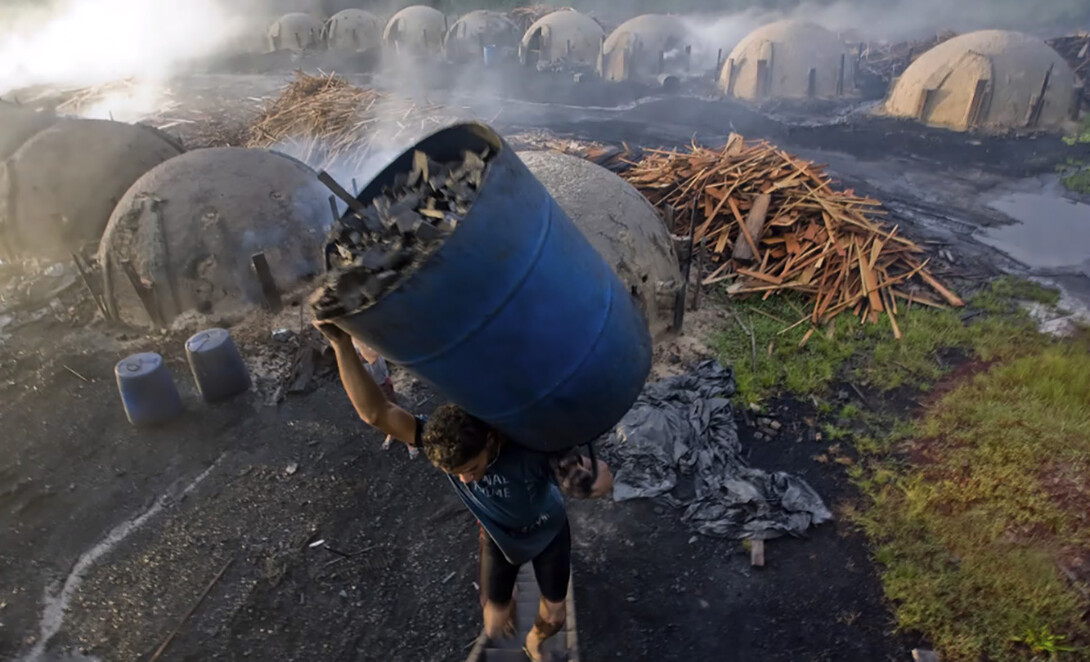 A slave carries a drum of burned wood to make charcoal in Brazil. Forests have been decimated in the country to create coal, which is then used for Brazil's steel industry. The forests are cut down and burned with slave labor.