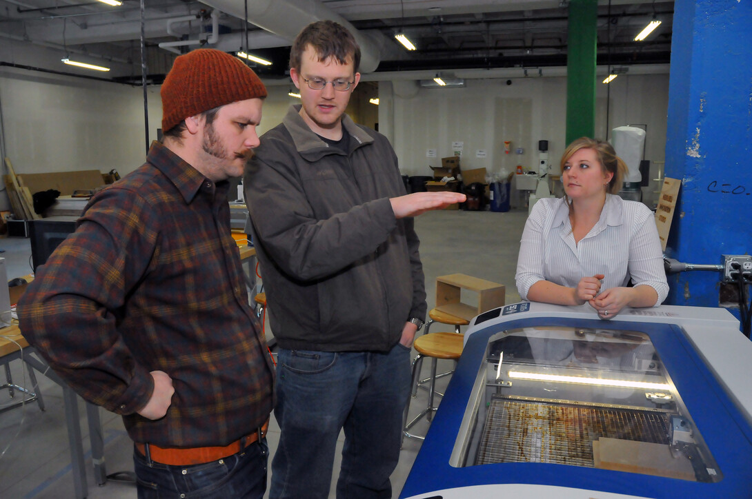 "Making for Innovation" student Byron Anway, (left) who is also an adjunct professor in art, and Liana Owad, (right) a UNL graduate and co-teacher in the course, listen as Tom Frederick talks about how a laser-guided cutting machine works.
