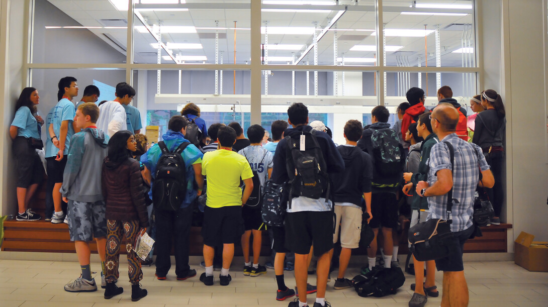 Students gather outside a Jorgensen Hall window to watch the Science Olympiad's sumo bots competition. The event pits robots designed by students against one another.