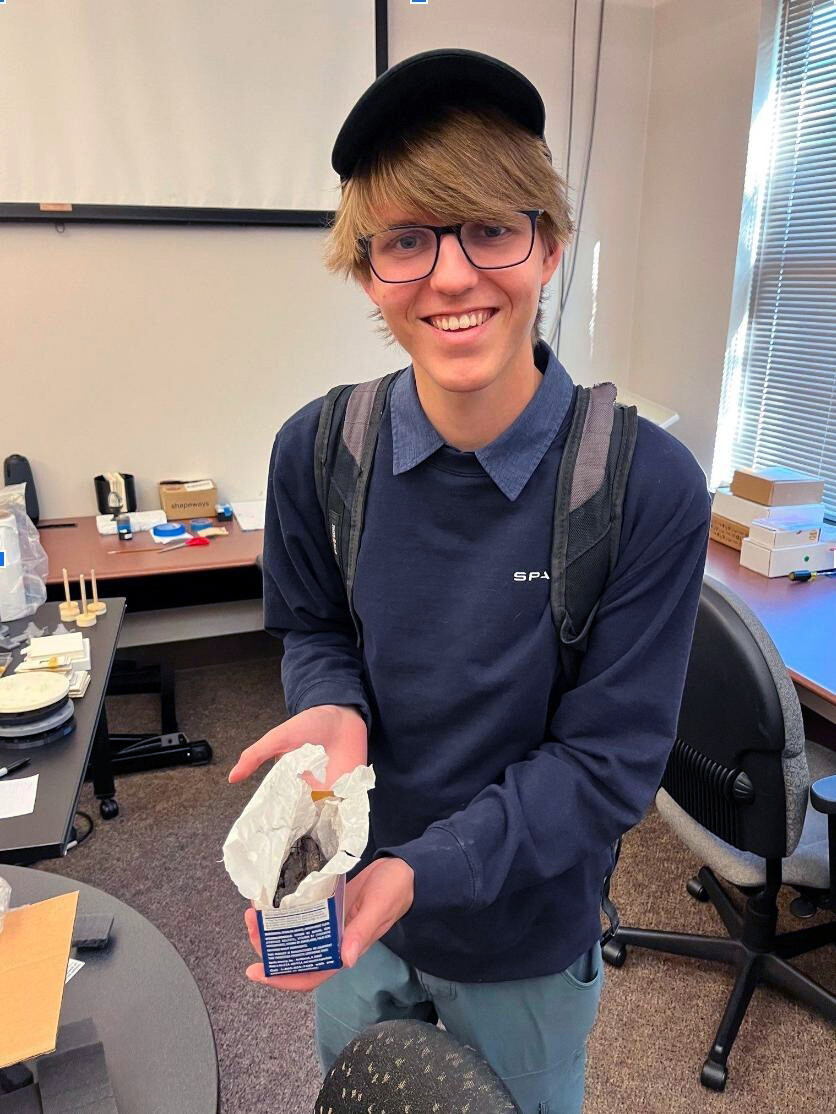 Luke Farritor holding a charred, simulated scroll similar to those recovered from Herculaneum