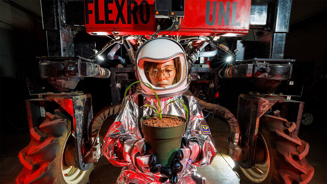 Katie Black wears a space suit costume while holding a potted corn plant