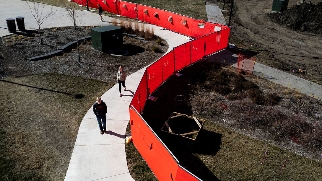 Students tread along a sidewalk bordered by a red-draped chain-link fence