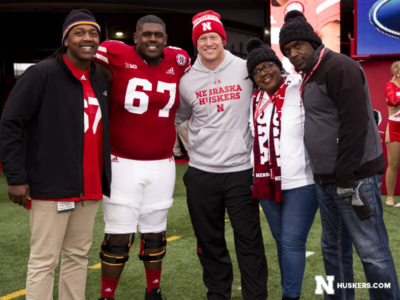 Charlie Foster poses for a photo with her husband and two sons and Coach Scott Frost