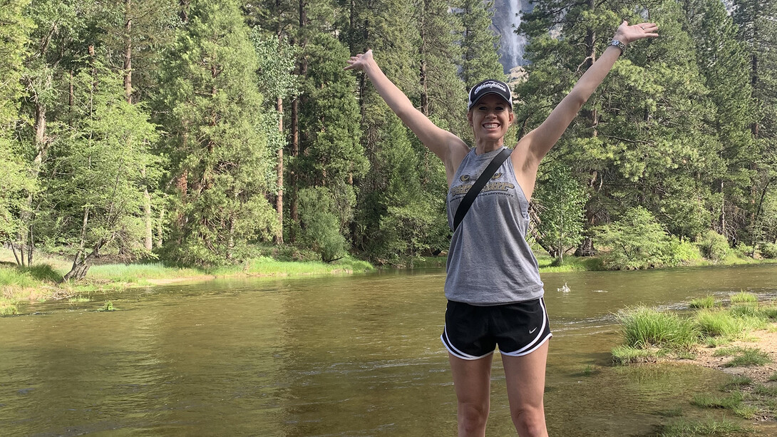 Nebraska's Kelcey Gabriel stands near a river with her arms in the air as a waterfall cascades down in the background.