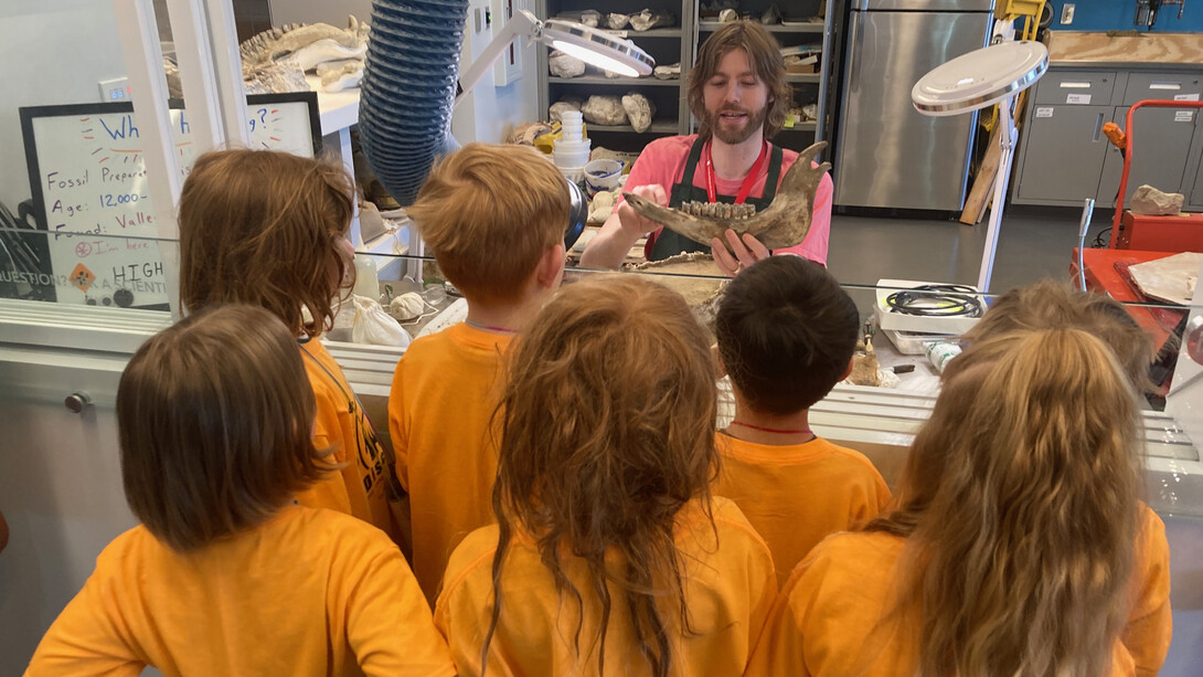 Six kids in yellow t-shirts gather around a man holding a fossilized jawbone with teeth.