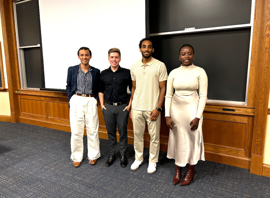 Four people stand in front of a blackboard.