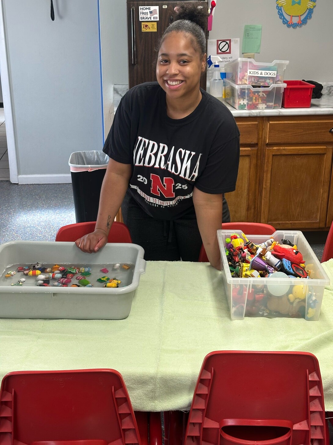 Jamiah Jackson in a black Nebraska t-shirt standing in front of a bucket of toys and a sanitizing tub.