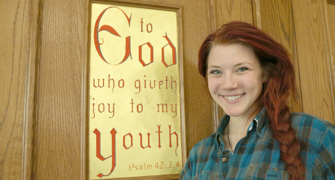 Anneleise Feldner, a sophomore art major, stands next to a Newman Center door panel she helped Bill Adair adorn with gold leaf and paint. 