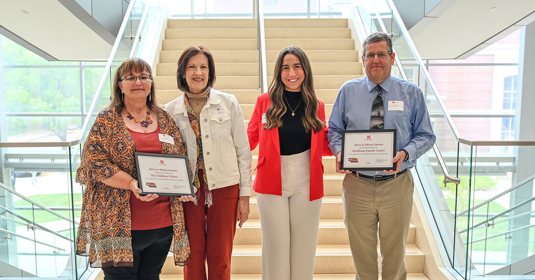 Kathy Majors in a red shirt and patterned cardigan with red hair and glasses, who holds a certificate, Kathy Paisley in red pants and a white jean jacket with short brown hair, Nikoleta Skoufis in white pants, a black turtleneck and a red blazer with long brown hair, and Curt Krueger in khakis, a blue shirt and tie and glasses, holding a certificate.