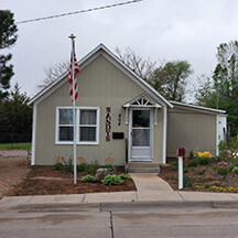 A small tan house with a sign depicting "Sandy" by the door.