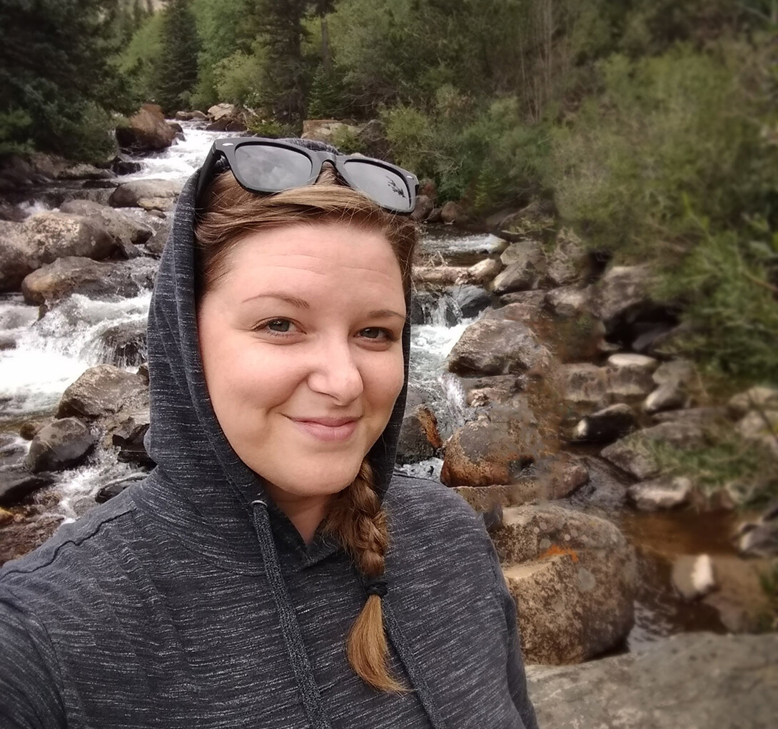 Alli Schultze walking by a river in the woods.