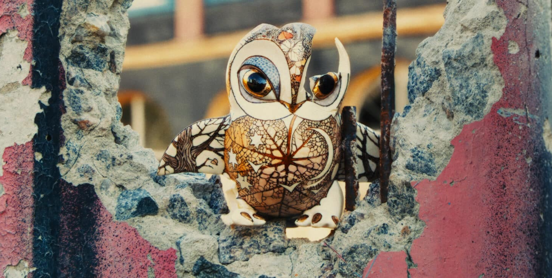 A film still from "Porcelain War" shows a ceramic painted owl with a bullet hole.