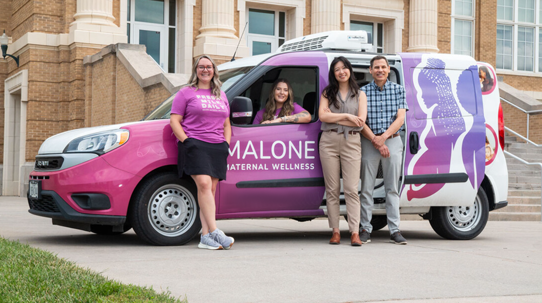 three people standing by the Malone Maternal Wellness car with a driver inside.