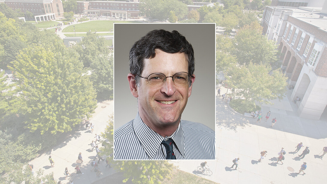 A headshot of David Sloss in a blue shirt and tie, with short brown hair and rectangular glasses.