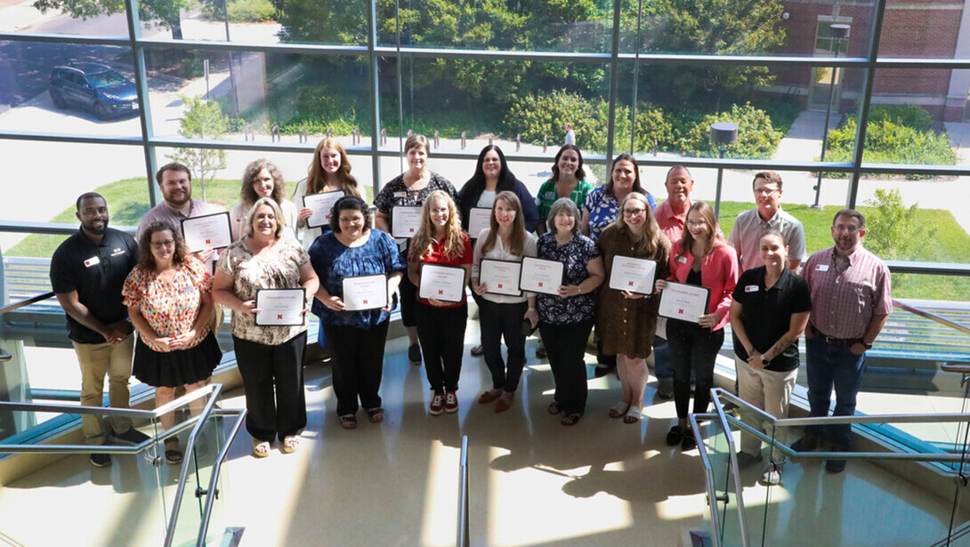Winners of past Staff Senate awards are pictured in front of a large window.