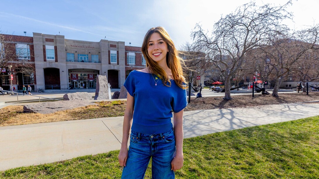 Ashley Mercer, co-director of Earthstock, stands in the green space outside the City Campus Union in a blue shirt and jeans. 