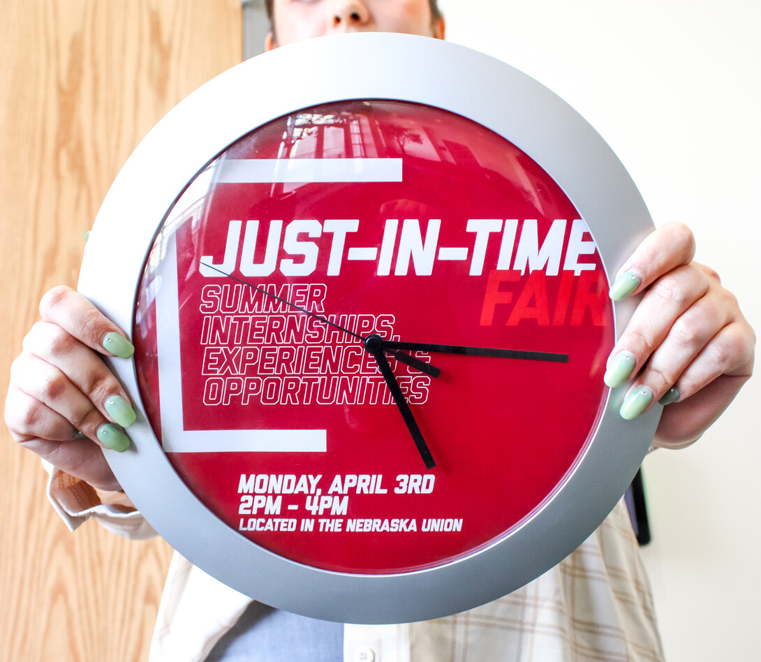 student holding clock with Just-In-Time fair details on the clock face.