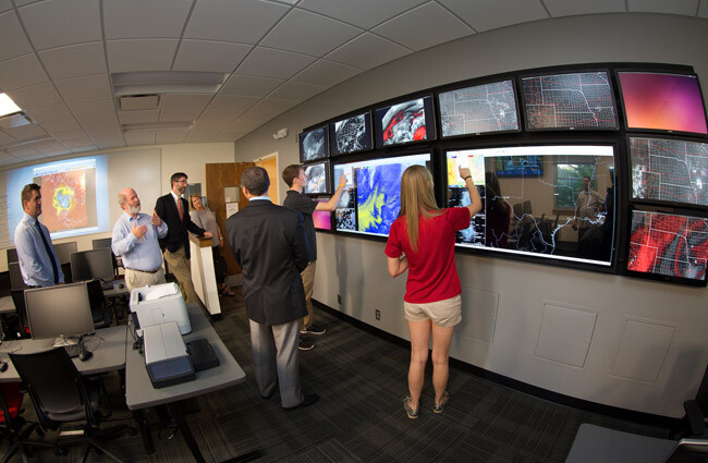 Clint Rowe, left, Professor of Earth & Atmospheric Sciences in the College of Arts and Sciences, describes the touch screen video wall.  Students demonstrated the wall during an open house for the newly remodeled Meteorology-Climatology Computer Lab in Bessey Hall.