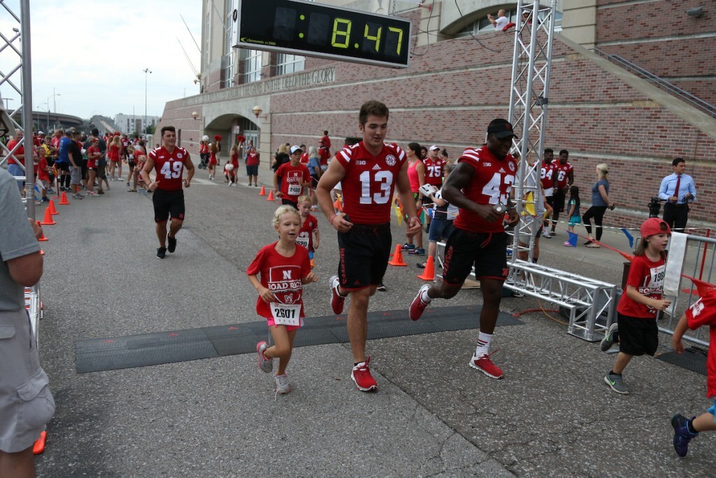 Huskers run alongside participants outside of Memorial Stadium in the Nebraska Football Road Race.