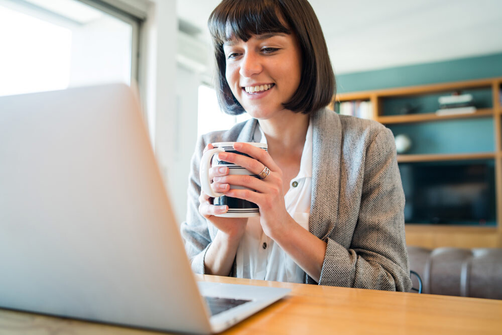 Women on laptop for virtual meeting holding coffee mug