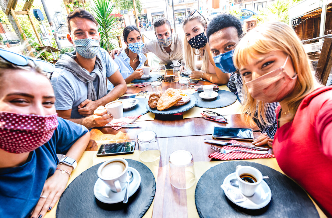 A group of friends meets up at a coffee house and takes a photo in masks.