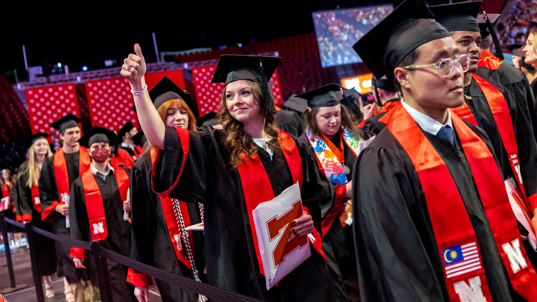 Leah Cemper, standing among fellow graduates, gives a thumbs-up to people in the crowd during the undergraduate commencement ceremony Dec. 20 at Pinnacle Bank Arena.